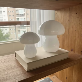 Dupla de cogumelos decorativos feitos de vidro branco em tamanhos de 17cm e 13cm, decorando estante de madeira.