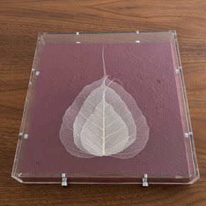 Encante-se com a delicadeza do quadro Folha Profunda. Folhas naturais meticulosamente esqueletizadas, emolduradas em acrílico sobre um fundo de papel artesanal.
