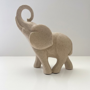 Perfil de escultura decorativa de elefante bege em poliresina com a tromba para cima, design minimalista e textura imitando pedra natural.