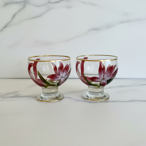 Conjunto de duas taças de vidro transparente pintadas à mão pela Artes Salles. Ambas exibem a mesma pintura floral marsala e fio de ouro nas bordas.