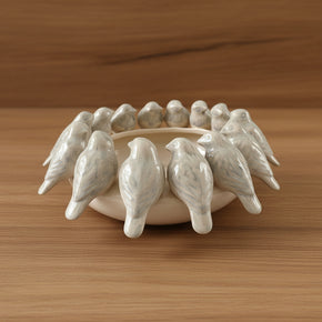 Peça decorativa de cerâmica com fileira de pequenos pássaros esculpidos na borda, destacando o design elegante e as nuances acinzentadas do esmalte.