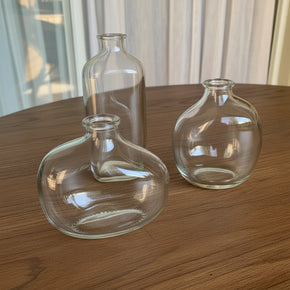 Trio de mini vasos de vidro com formato orgânico e assimétrico da So Sweet Kasa, dispostos vazios sobre uma mesa de madeira em ambiente iluminado.