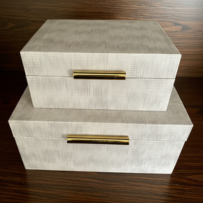 Conjunto com 2 caixas decorativas em madeira e couro sintético cinza claro e ferragens douradas.