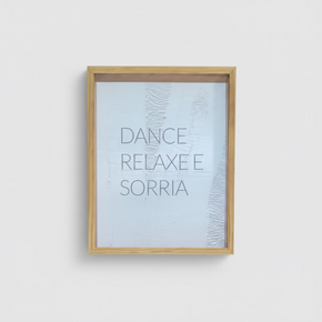 Quadro decorativo retangular com moldura de madeira clara e fundo texturizado branco em relevo, exibindo a frase minimalista 'DANCE, RELAXE E SORRIA' centralizada.