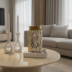 Potiche decorativo de cerâmica com estampa de zebra com fundo branco e estampa dourada, medindo 26 cm de altura. Tem tampa dourada. Está posicionado sobre uma mesa de centro. À venda na o Sweet Kasa.