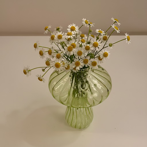 Mini vaso verde em vidro e formato de cogumelo com arranjo de pequenas margaridas.
