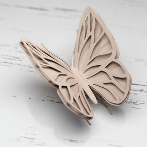 Adorno de borboleta em metal na cor rosé, com asas vazadas em duas camadas e acabamento fosco, apoiada sobre uma superfície clara.