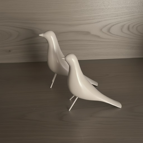 Vista de dois pássaros decorativos minimalistas em resina nude rosado com patas de metal, posicionados sobre superfície de madeira escura.