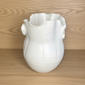 O vaso de cerâmica off white com micropigmentos, formato orgânico escultural em nicho de móvel de madeira.