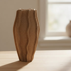 Vaso de cerâmica cor marrom claro com formato orgânico e linhas verticais onduladas, apresentando acabamento fosco e textura rústica que imita areia, em fundo branco para a loja So Sweet Kasa.
