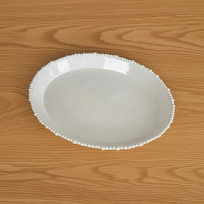 Vista superior de uma travessa oval grande em melamina premium da linha Vanilla Pearl, mostrando o fundo off-white com efeito salpicado e a borda decorada com pérolas.